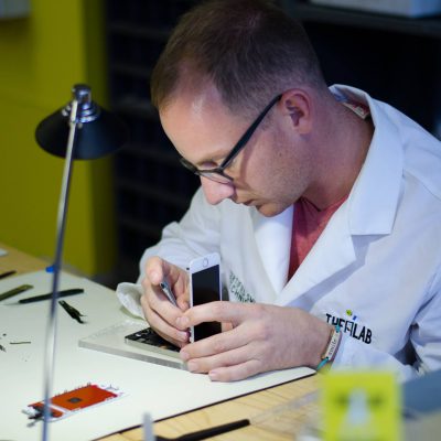 alt+"lyle schrock sitting at a table at the lab in warsaw fixing a cell phone screen